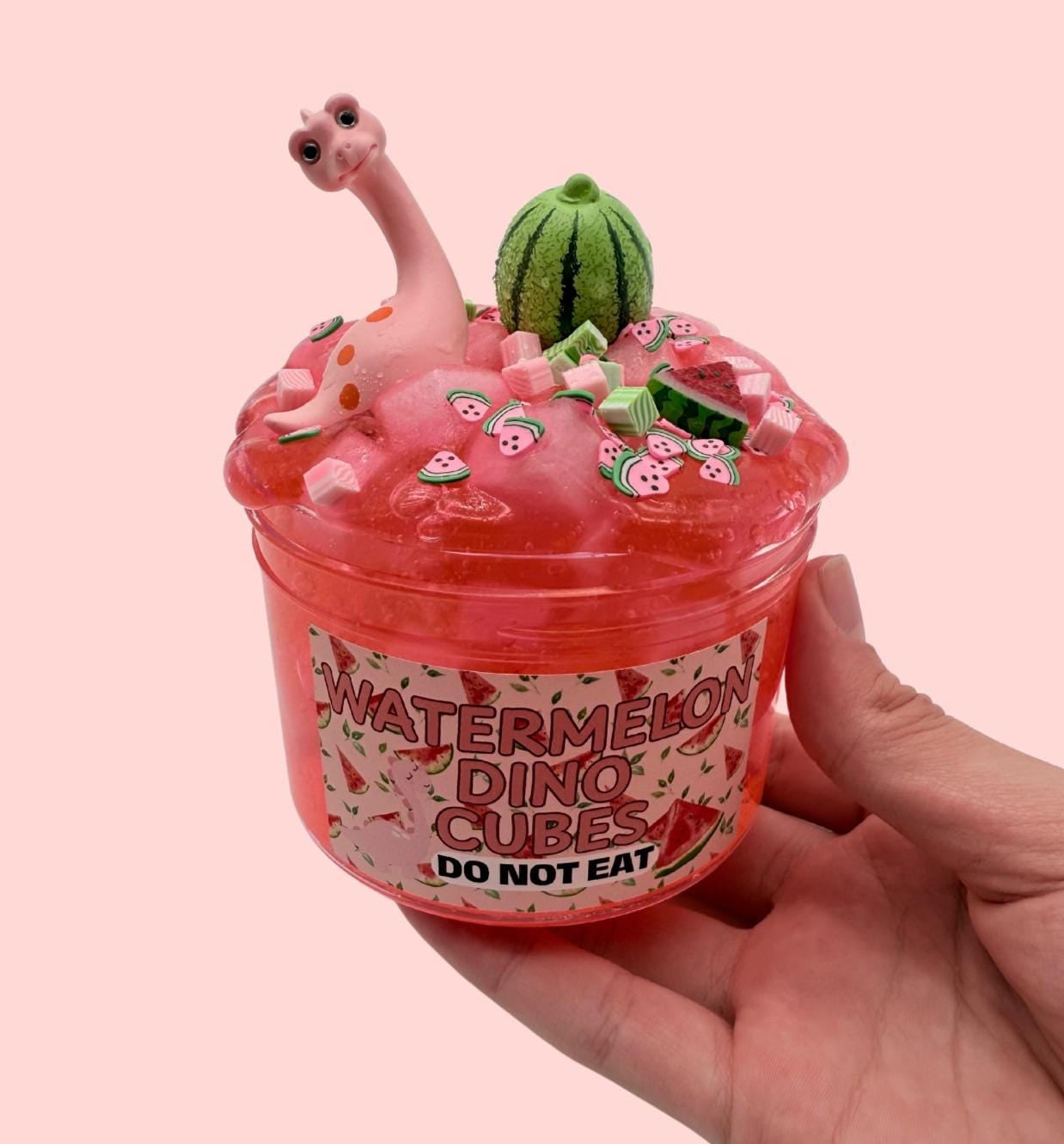 Hand holding a container of 'Watermelon Dino Cubes' with a pink background