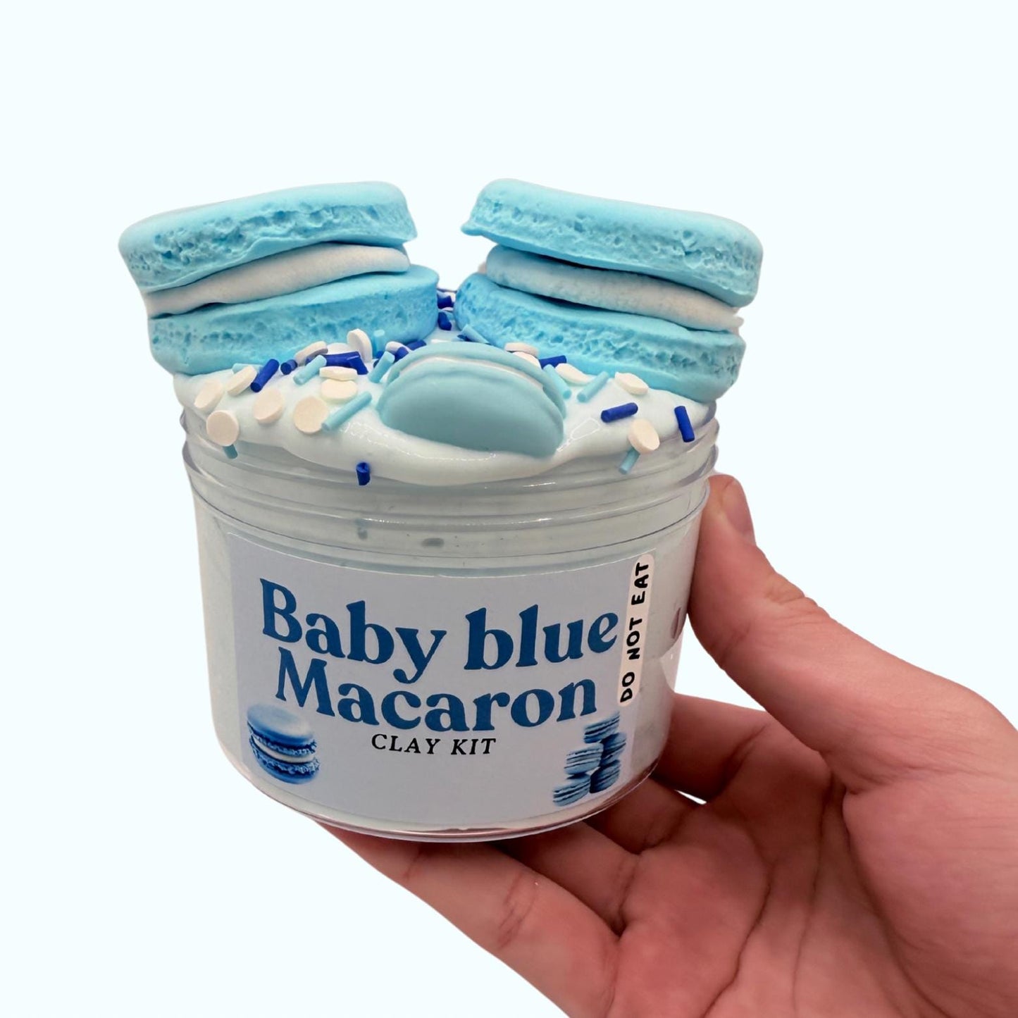 Hand holding a 'Baby Blue Macaron Clay Kit' with blue macaron decorations on a white background